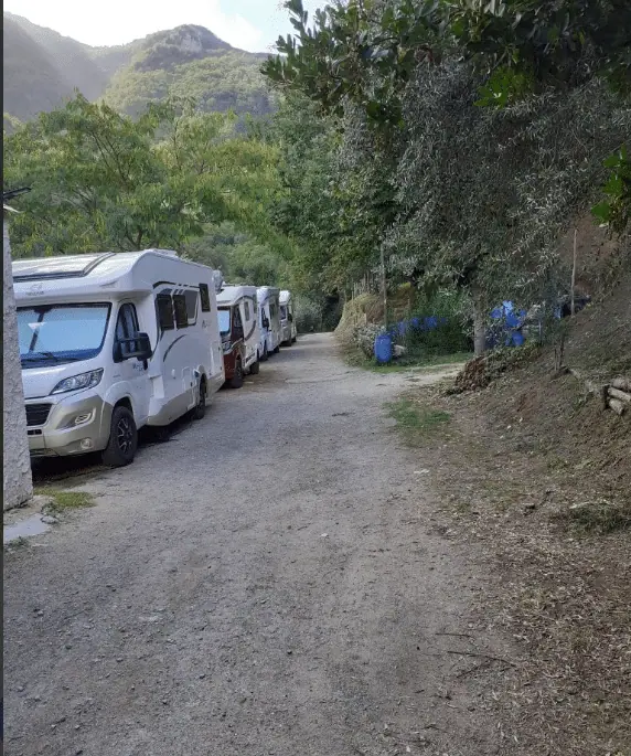 Obytná auta na prašné cestě pod stromy v malém autokempu La Divina nad Amalfi