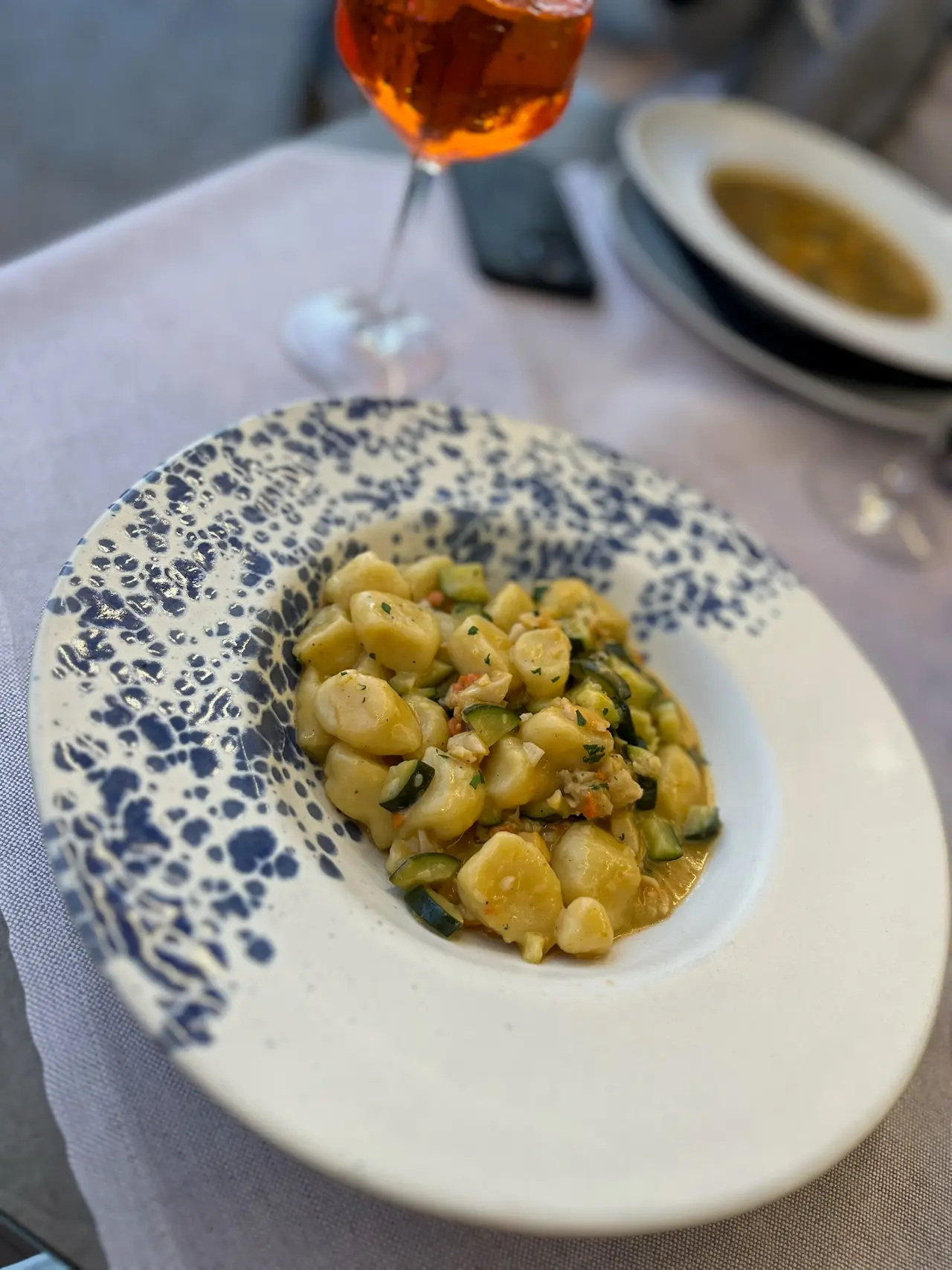 Gnocchi s cuketou a mořskými plody, za nimi Aperol spritz a minestrone v restauraci v Caorle