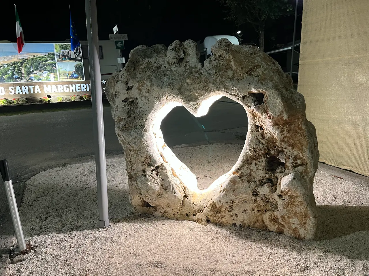 Osvětlený kámen s vyřezaným srdcem večer u vstupu do kempu Santa Margherita