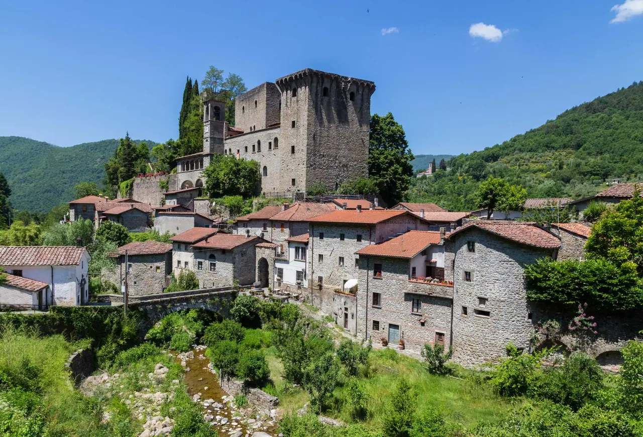 Mohutný středověký hrad Castello della Verrucola s kulatou věží dominuje kamenné vesnici Fivizzano v údolí řeky mezi zelenými kopci Toskánska