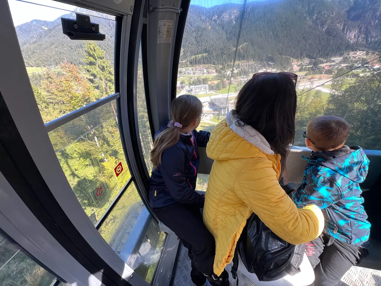 Monika s dětmi v kabince lanovky na Monte Lussari se dívají z okna do údolí