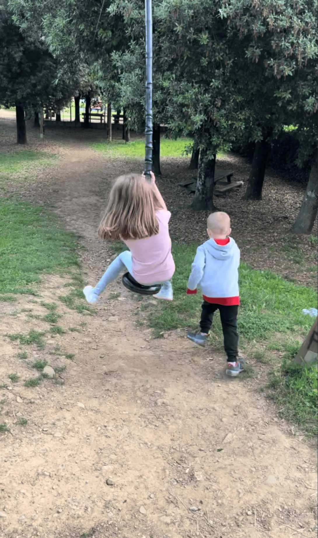 Naše děti si hrají na dětském hřišti ve Fivizzanu, holčička na houpačce a chlapeček v modré mikině pozoruje okolí