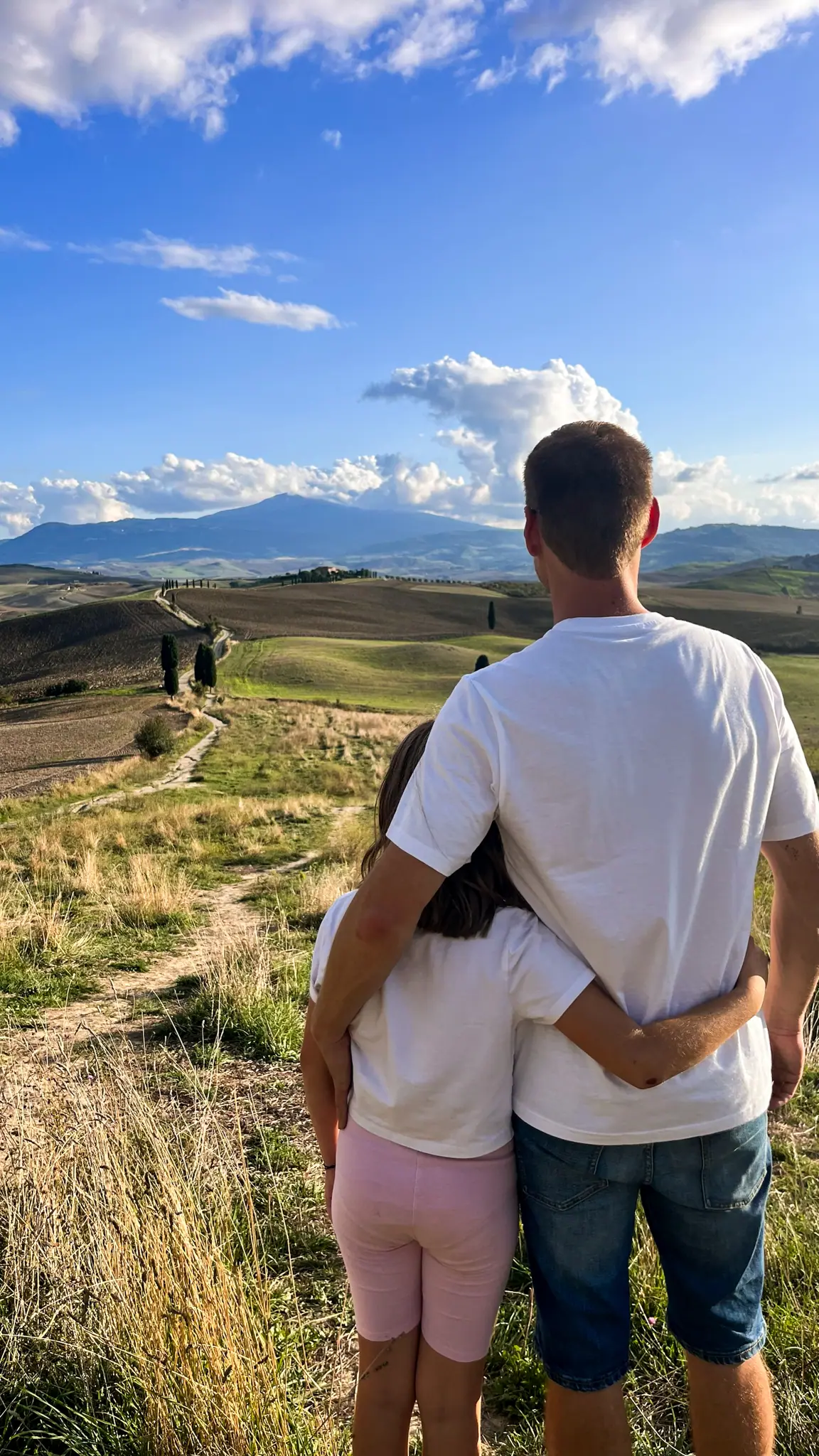 Otec objímá svou dceru a společně hledí na ikonickou krajinu Gladiator Point ve Val d’Orcia.