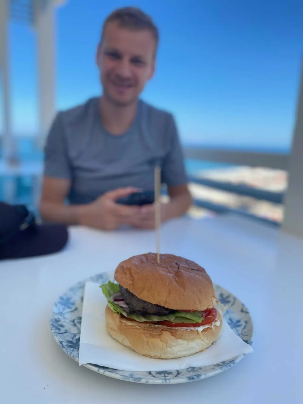 Martin s hamburgerem u stolu v restauraci u pláže v Tropei s výhledem na moře