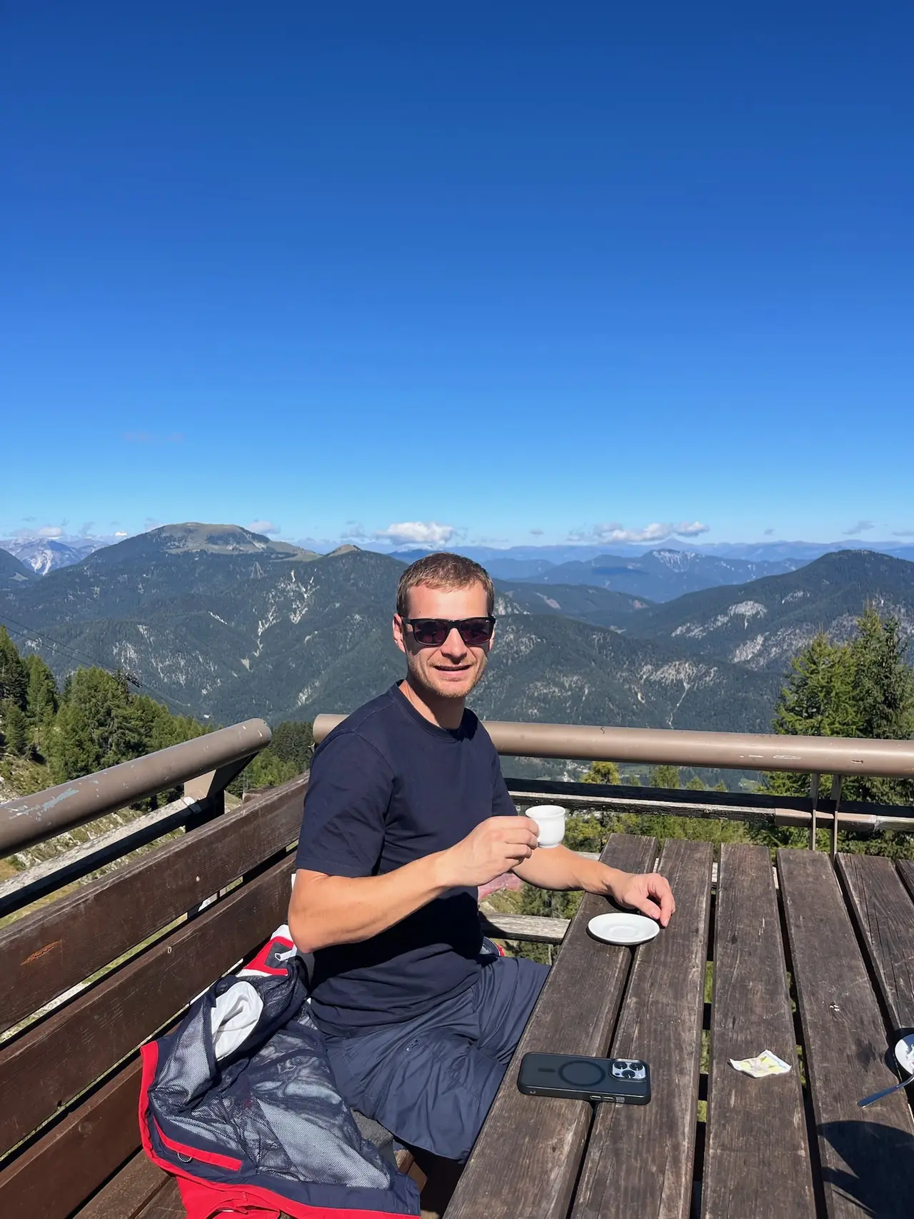 Martin s kávou na terase na Monte Lussari, za ním horizont Julských Alp