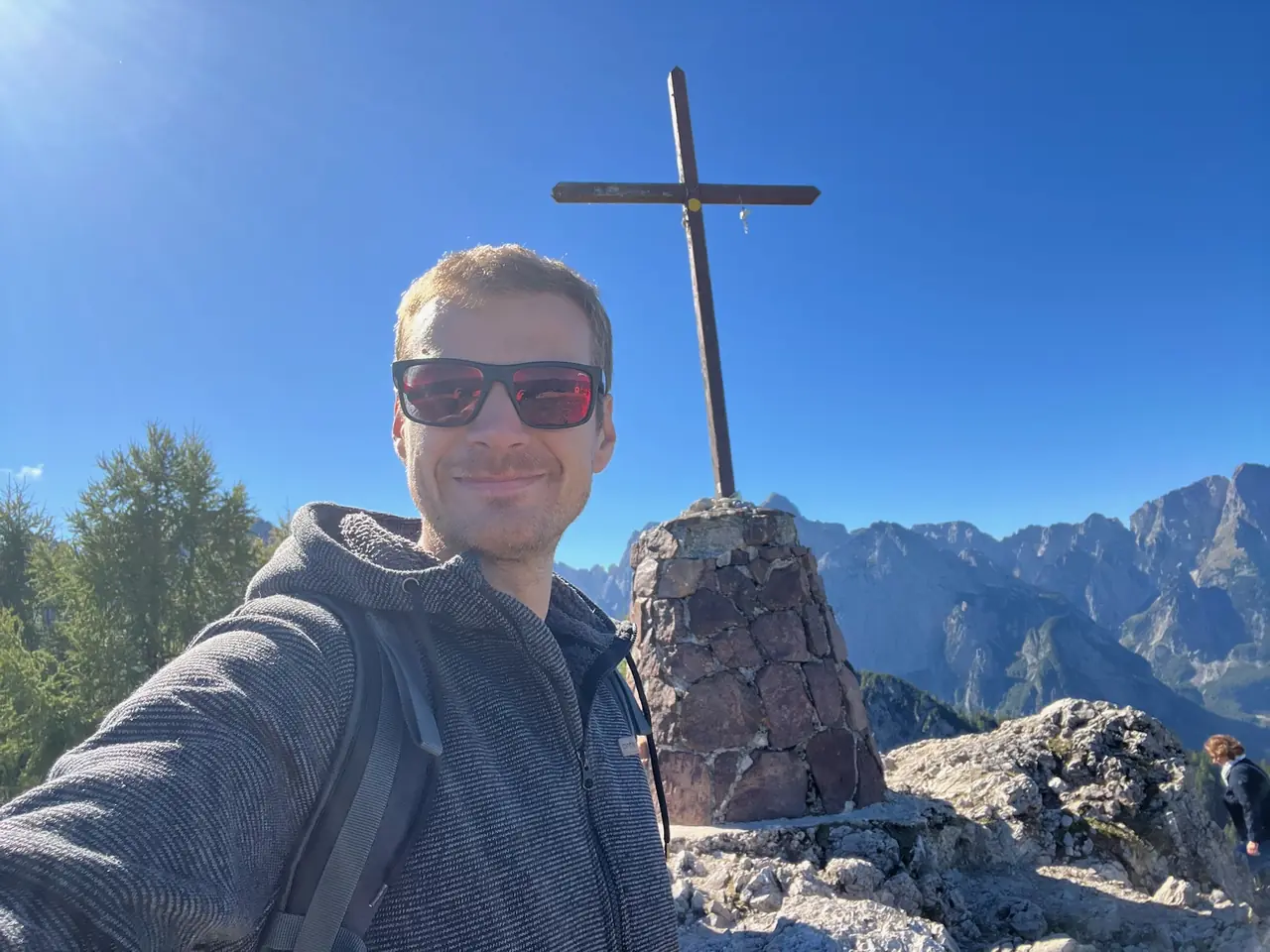 Martin se selfie u dřevěného kříže na vrcholu Monte Lussari, za ním hory