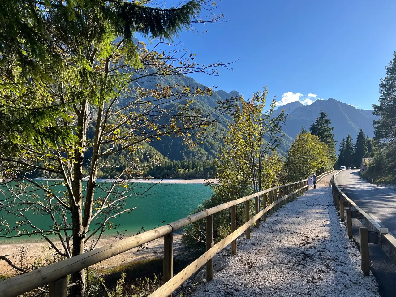 Dřevěné zábradlí stezky podél silnice nad Lago del Predil, vlevo tyrkysové jezero