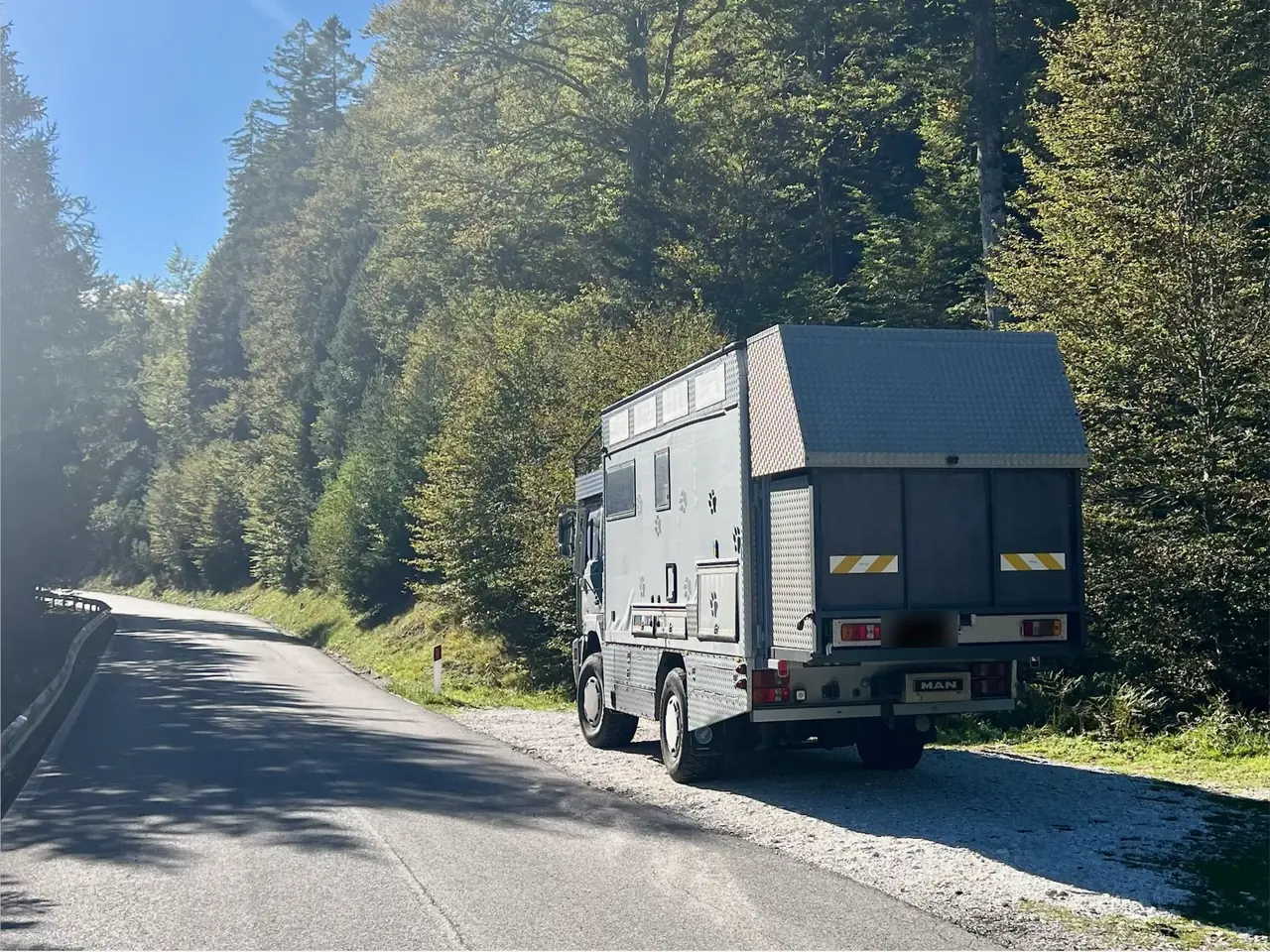 Šedé expediční nákladní auto MAN zaparkované u silnice v lese u Lago del Predil