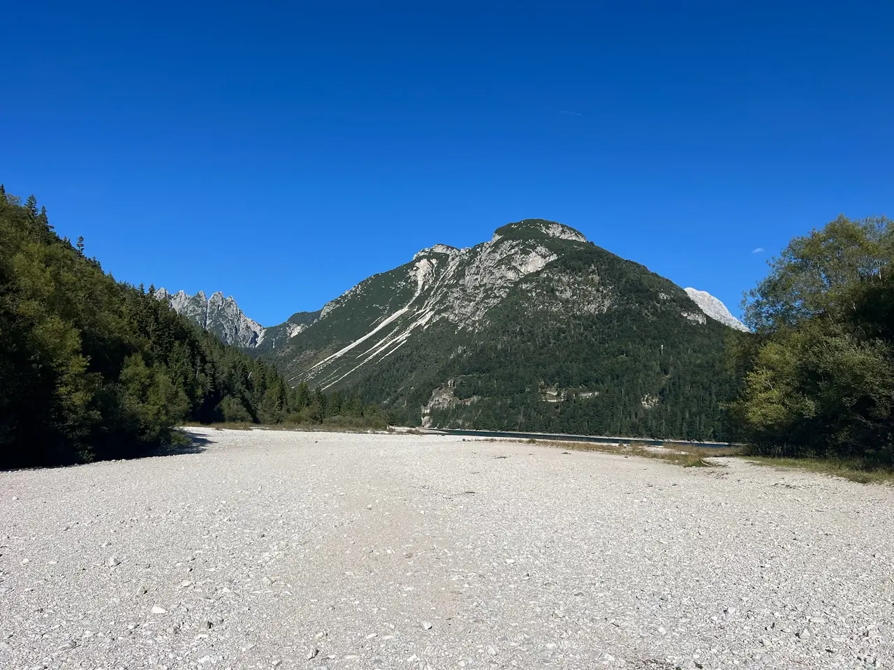 Široký pruh suchých oblázků u Lago del Predil při nízké hladině, v pozadí hora