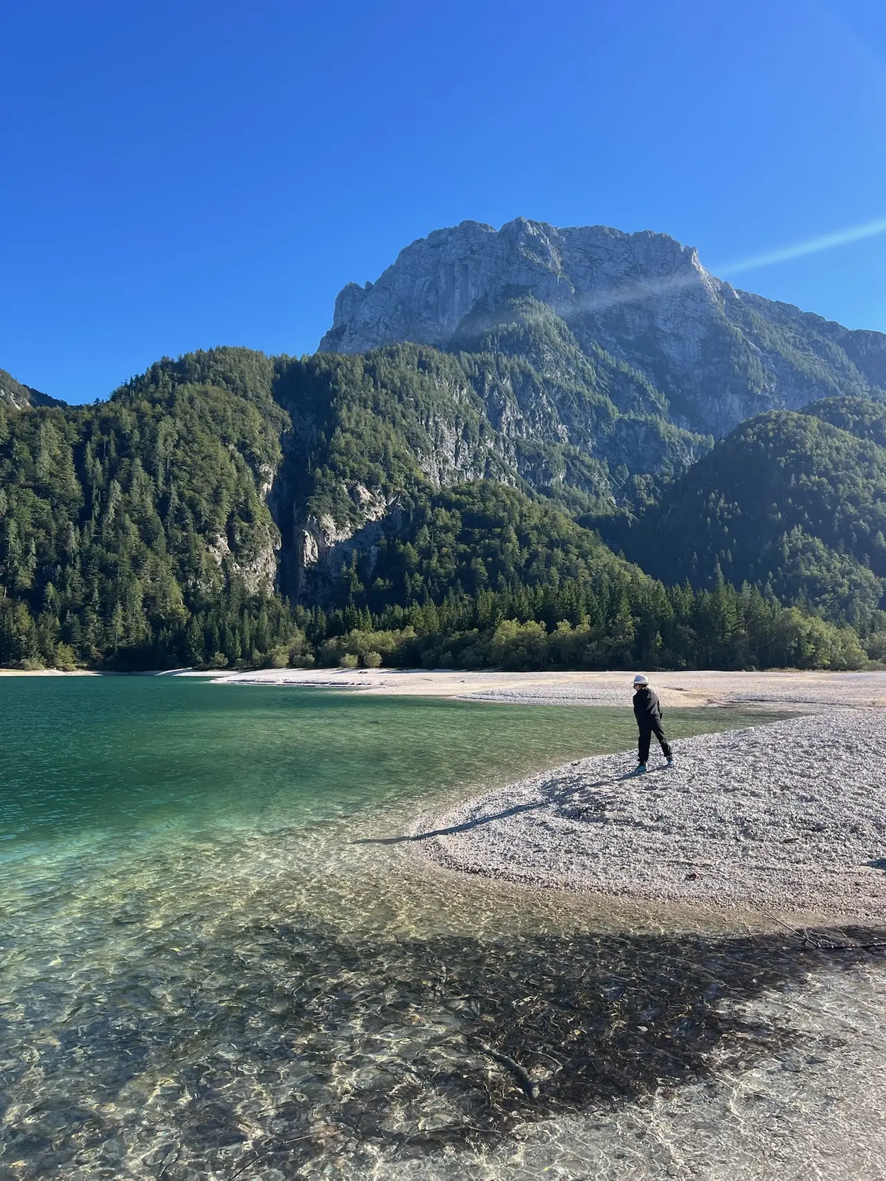 Procházka po oblázkovém okraji Lago del Predil při nízké hladině, vzadu hory
