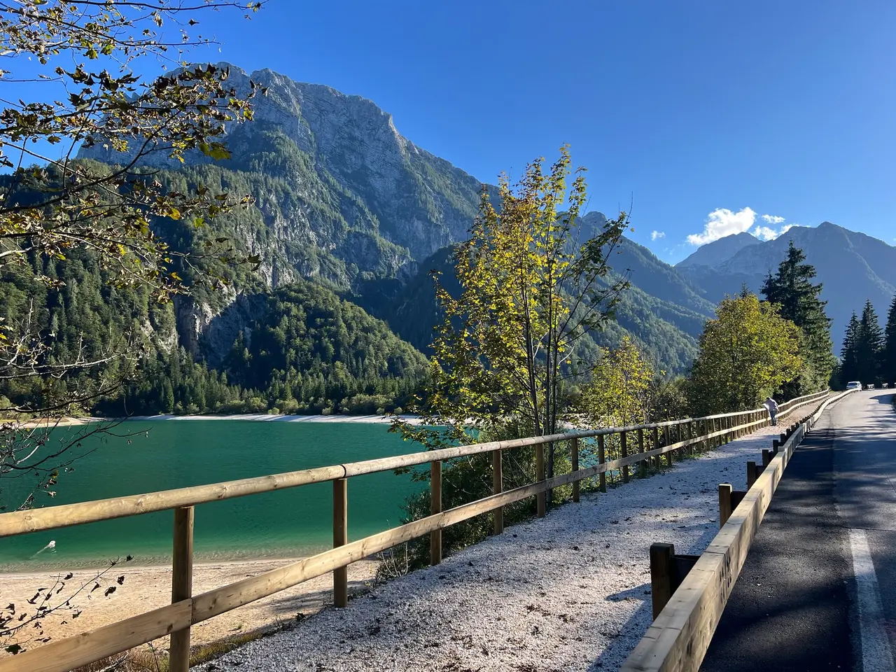 Stezka s dřevěným zábradlím nad Lago del Predil a skalnaté hory v podzimním slunci