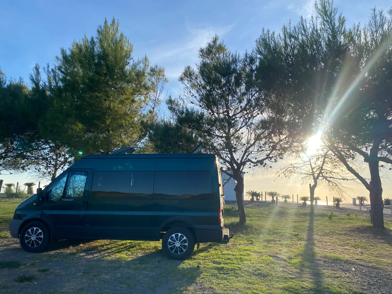 Naše dodávka Ford Transit pod borovicemi v kempu v Castrocuccu u Maratey při západu slunce