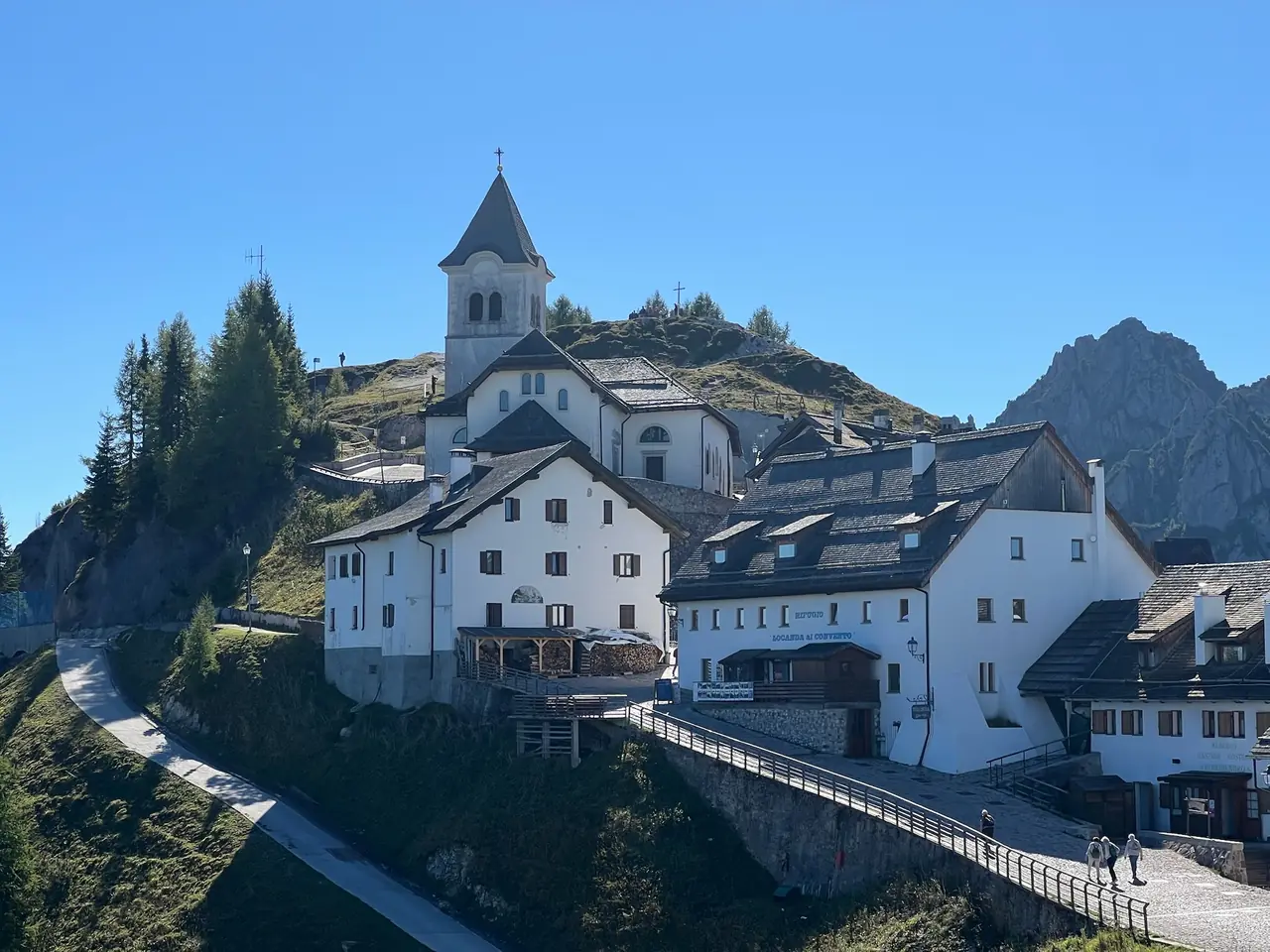 Bílé domy horské osady Monte Lussari a svatyně se zvonicí na vrcholu, vlevo kamenná cesta