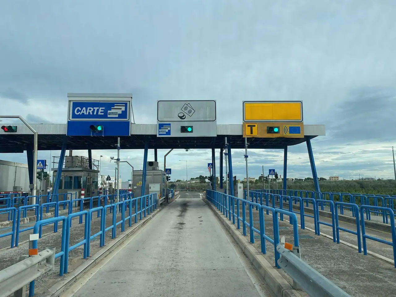 Průjezd mýtnou bránou na italské dálnici s modrými zábradlími a značkami pro platbu kartou, hotovost a telepass