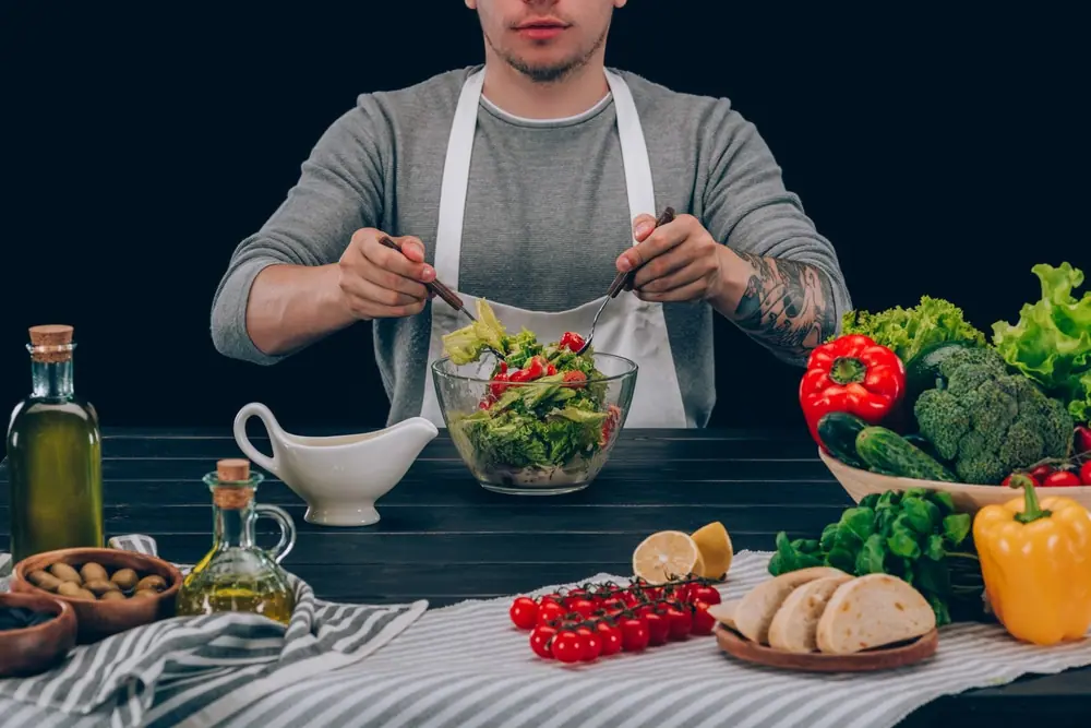 Muž míchá salát na stole s olivovým olejem a zeleninou