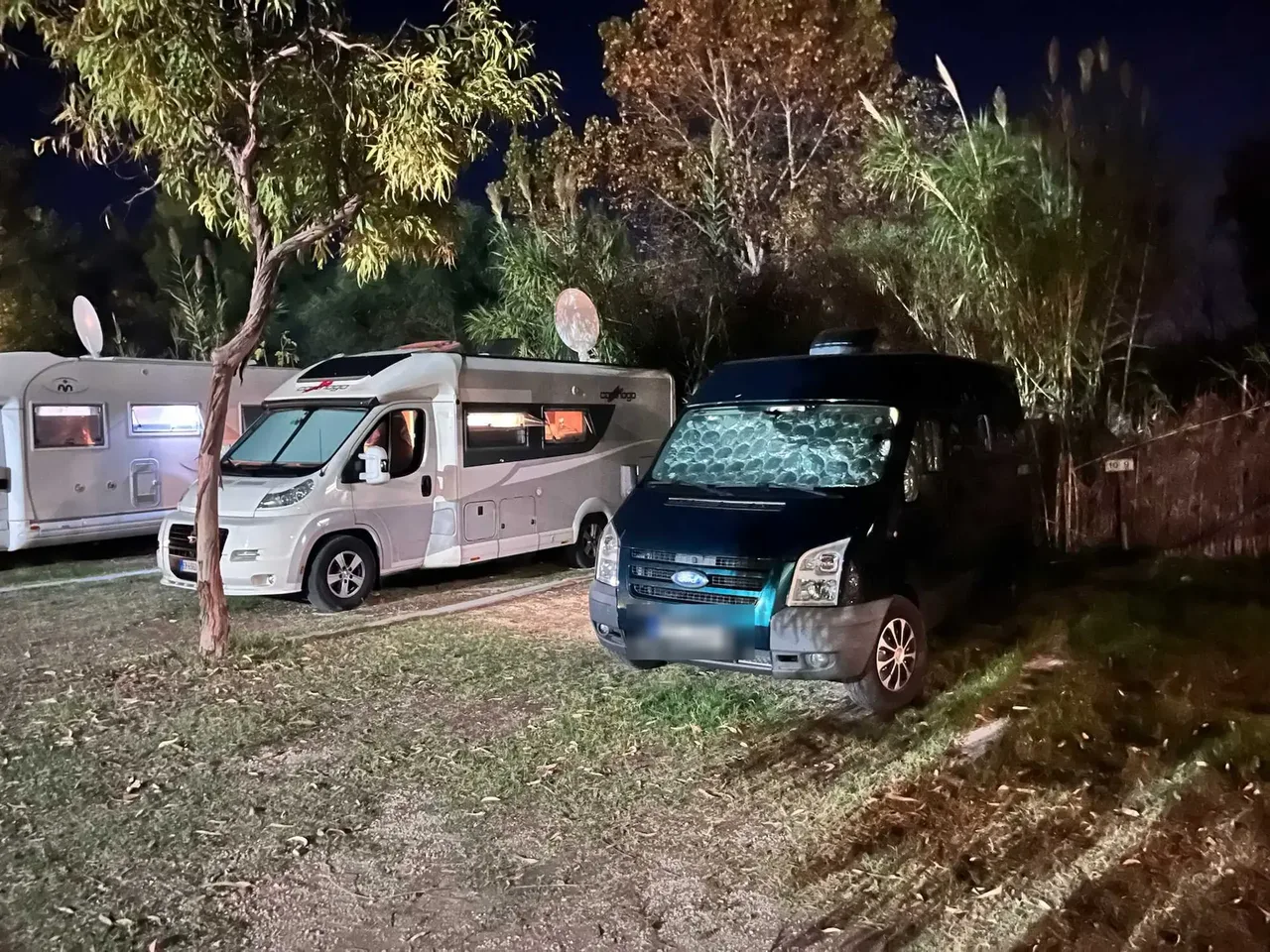 Náš obytný vůz a karavany zaparkované na travnatém kempu ve Vieste během teplé večerní noci pod stromy