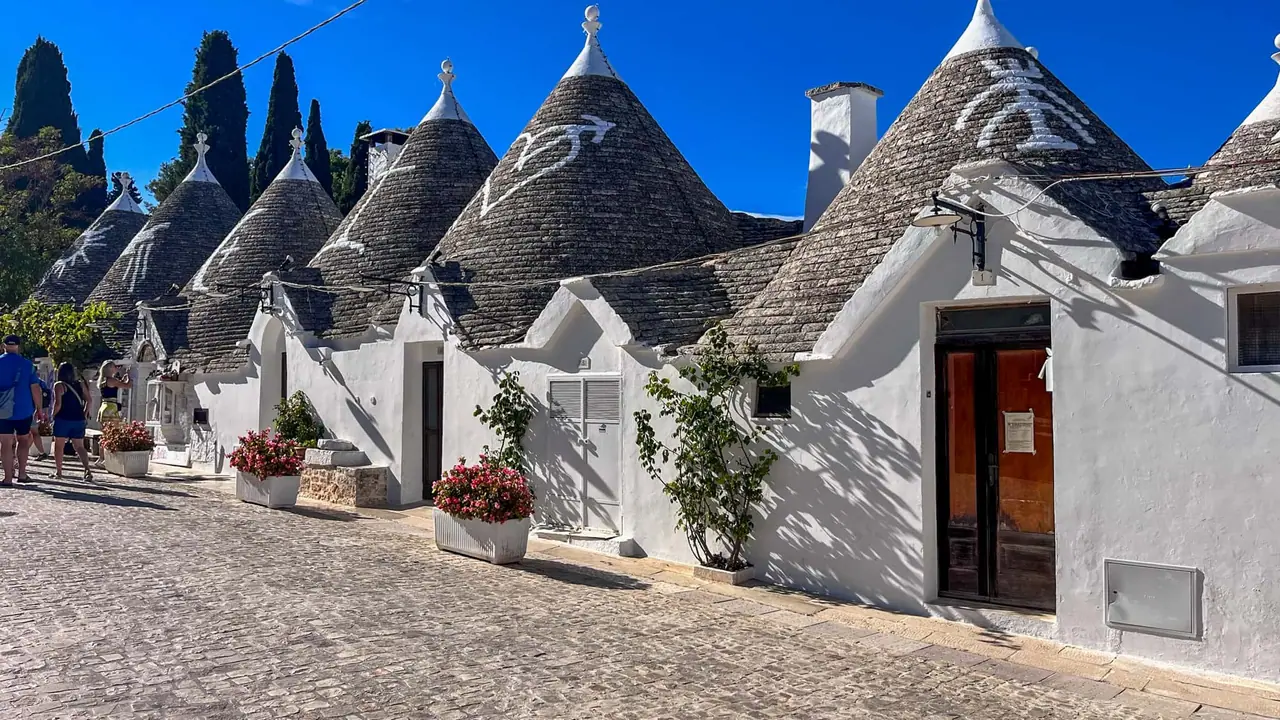 Řada bílých trulli domečků s kuželovitými střechami a červenými dveřmi v historické čtvrti Rione Monti v Alberobellu
