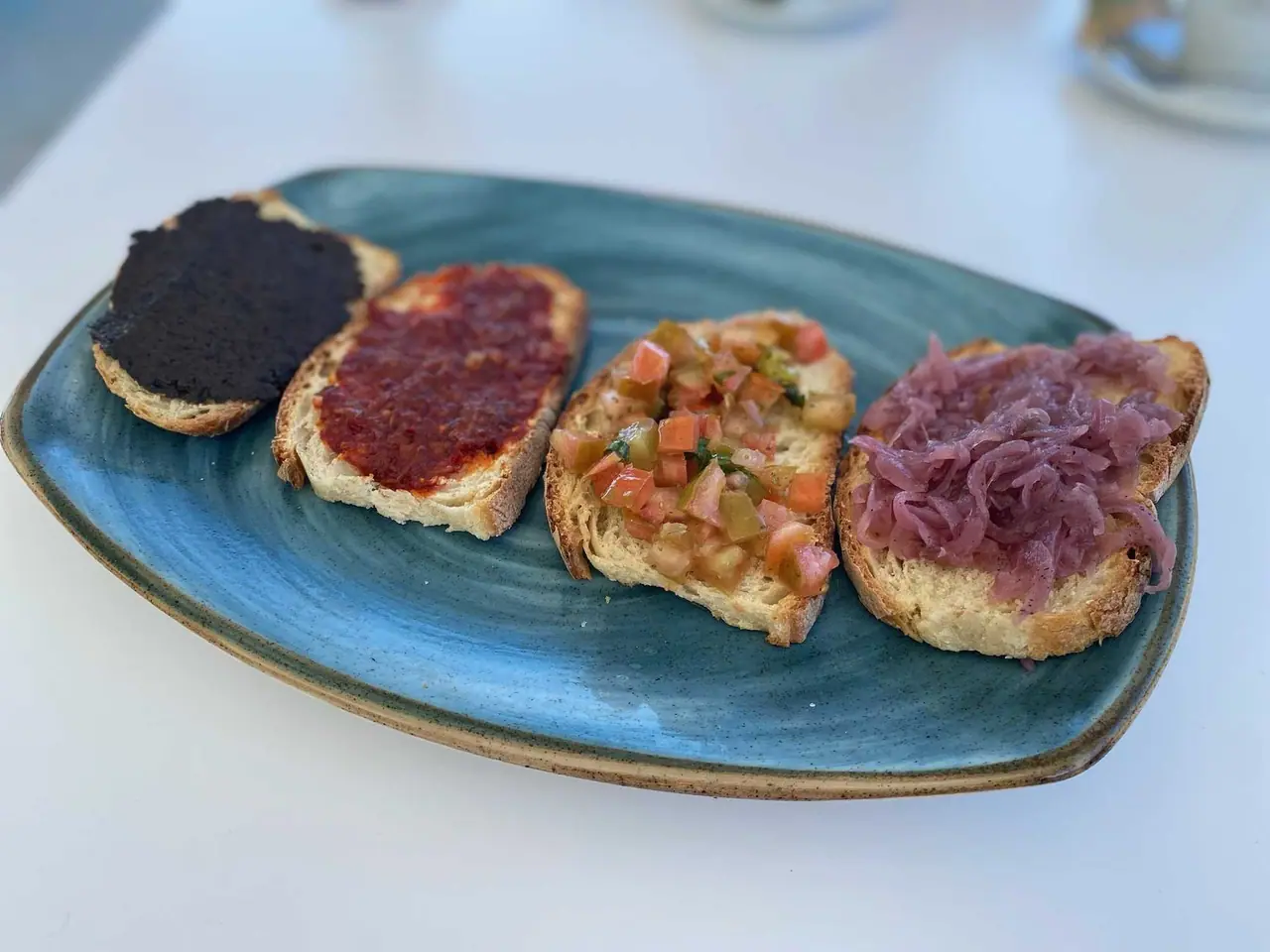 Čtyři bruschetty na modrém talíři v restauraci u pláže v Tropei