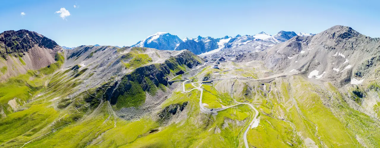 Serpentiny průsmyku Stelvio mezi zelenými svahy a zasněženými štíty Alp