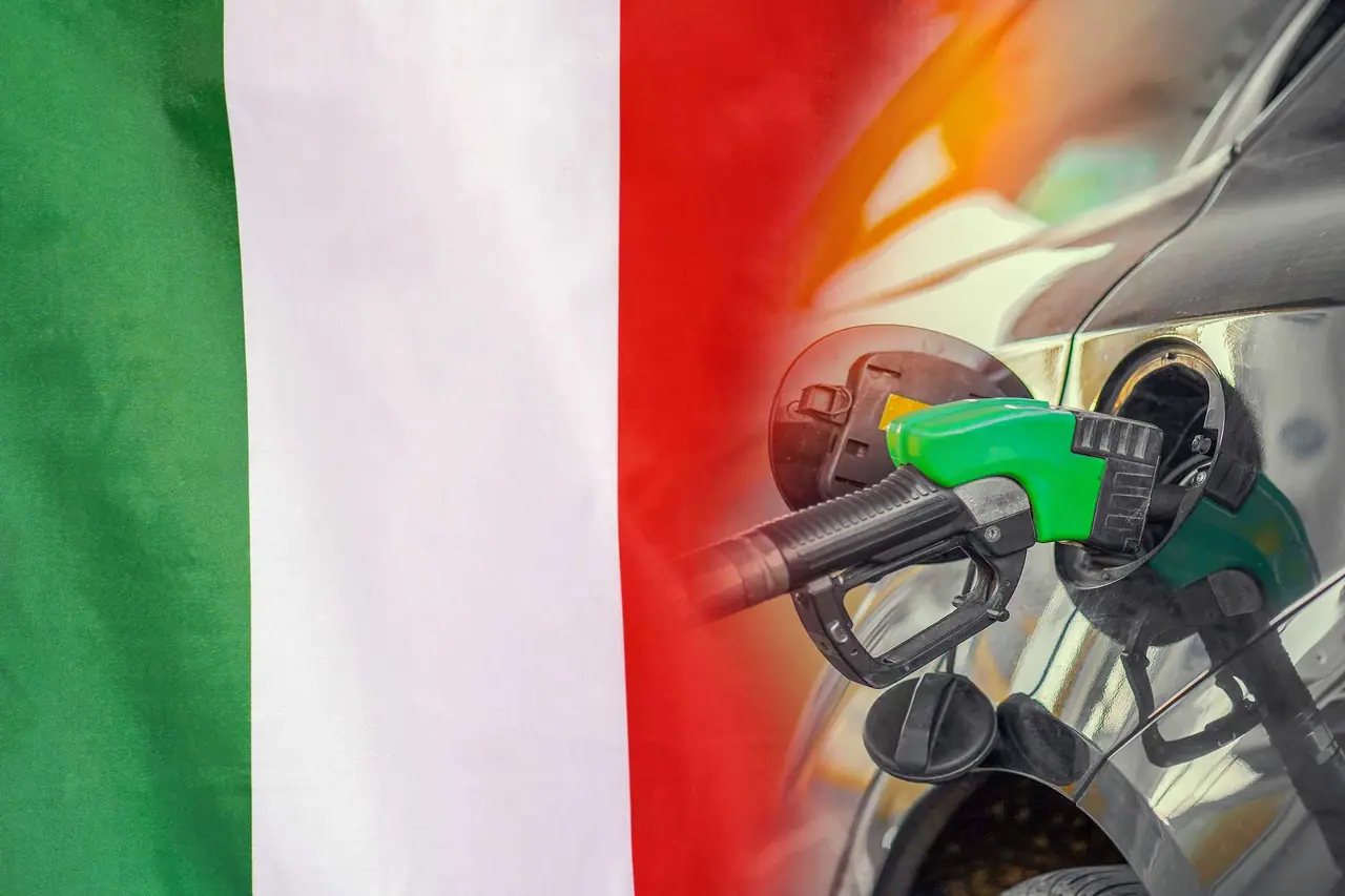 Zelená benzínová pistole zasunutá do nádrže tmavého auta na pozadí italské trikolóry v zelené, bílé a červené barvě.
