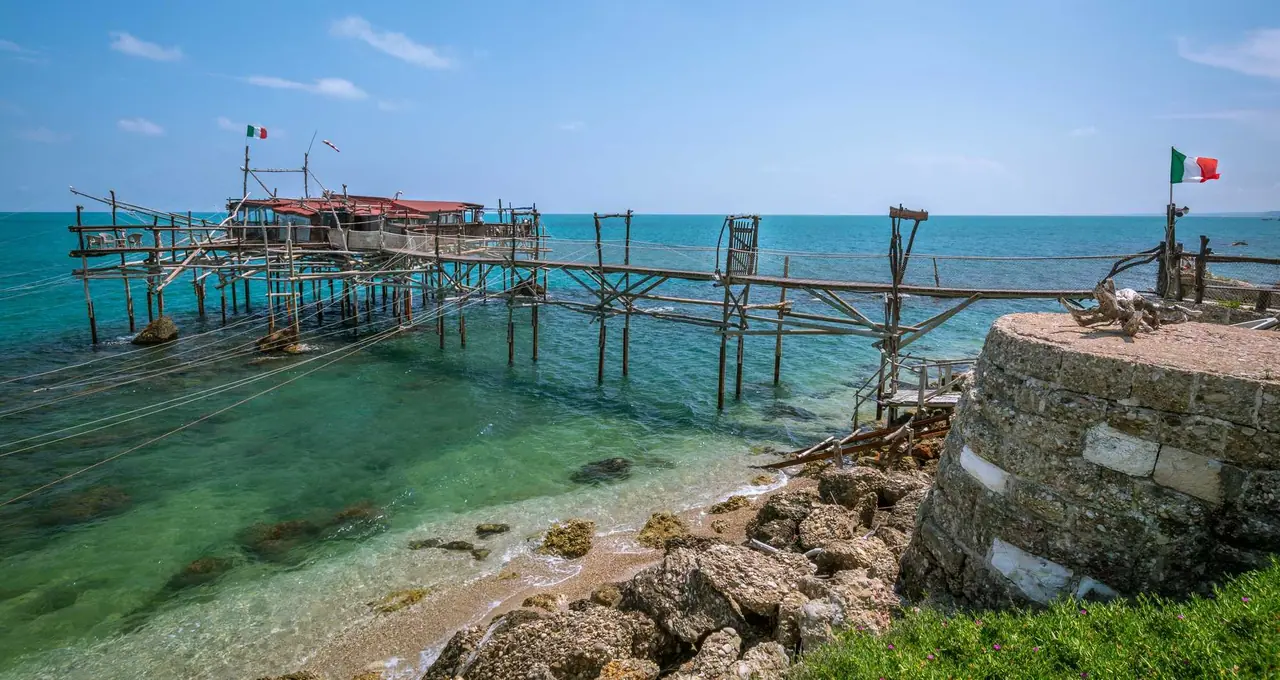 Tradiční dřevěná rybářská platforma trabocco na Jadranském moři s italskými vlajkami a tyrkysovou vodou v Abruzzách