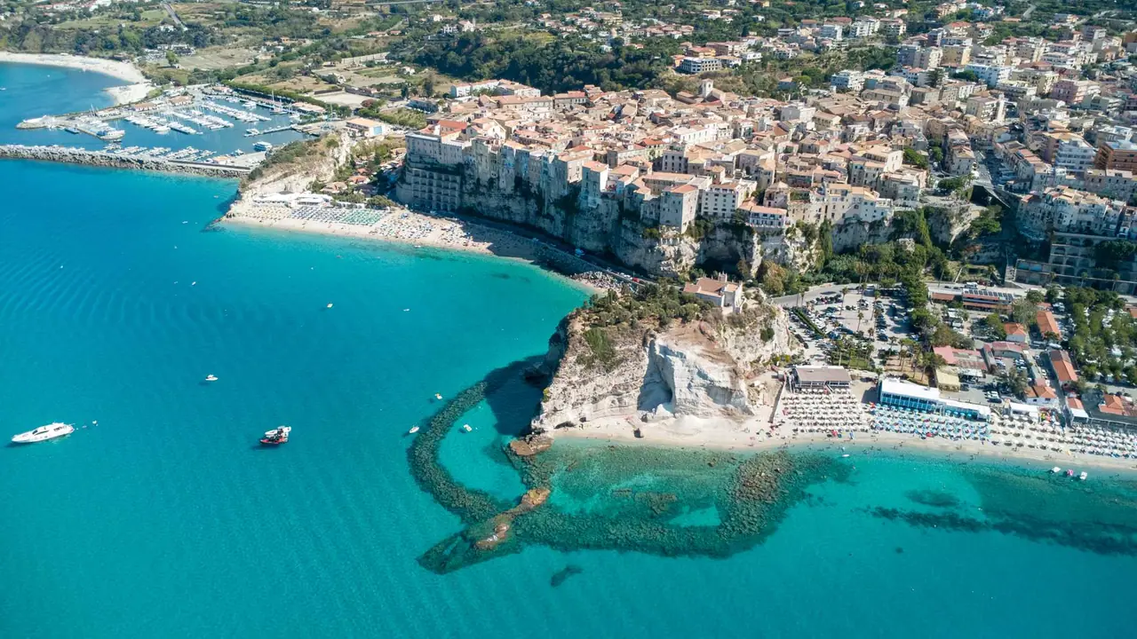 Letecký pohled na Tropeu s domy na útesu, skálou se svatyní Santa Maria dell'Isola a pláží u tyrkysového moře