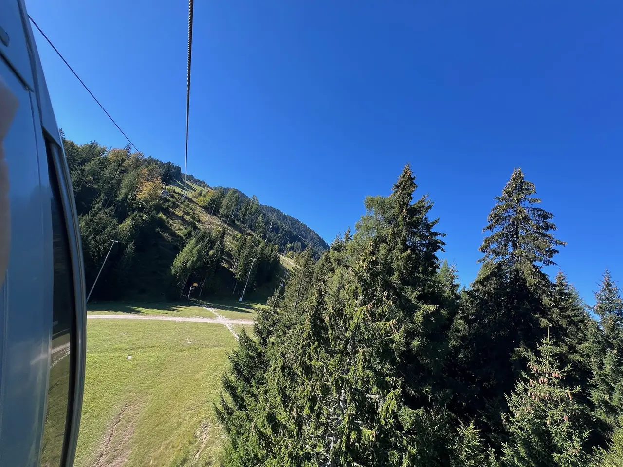 Pohled z kabinky lanovky na lesnatý svah a louky pod Monte Lussari