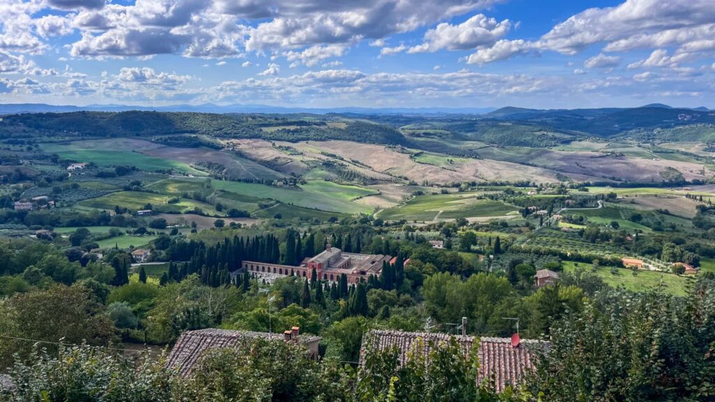 Výhled z Montepulciana na rozlehlou toskánskou krajinu s vinicemi, cypřiši a červenými střechami domků v údolí