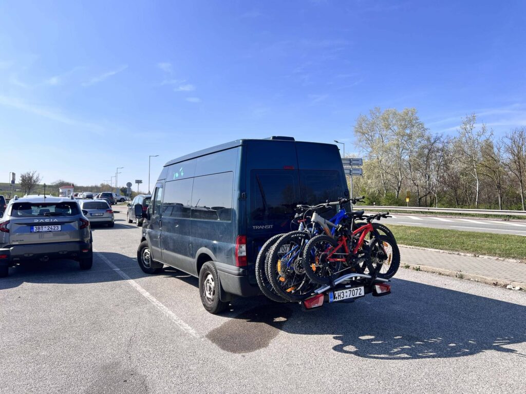Náš šedý Ford Transit s nosičem Thule na tažném háku se čtyřmi koly stojí v dopravní zácpě na dálnici