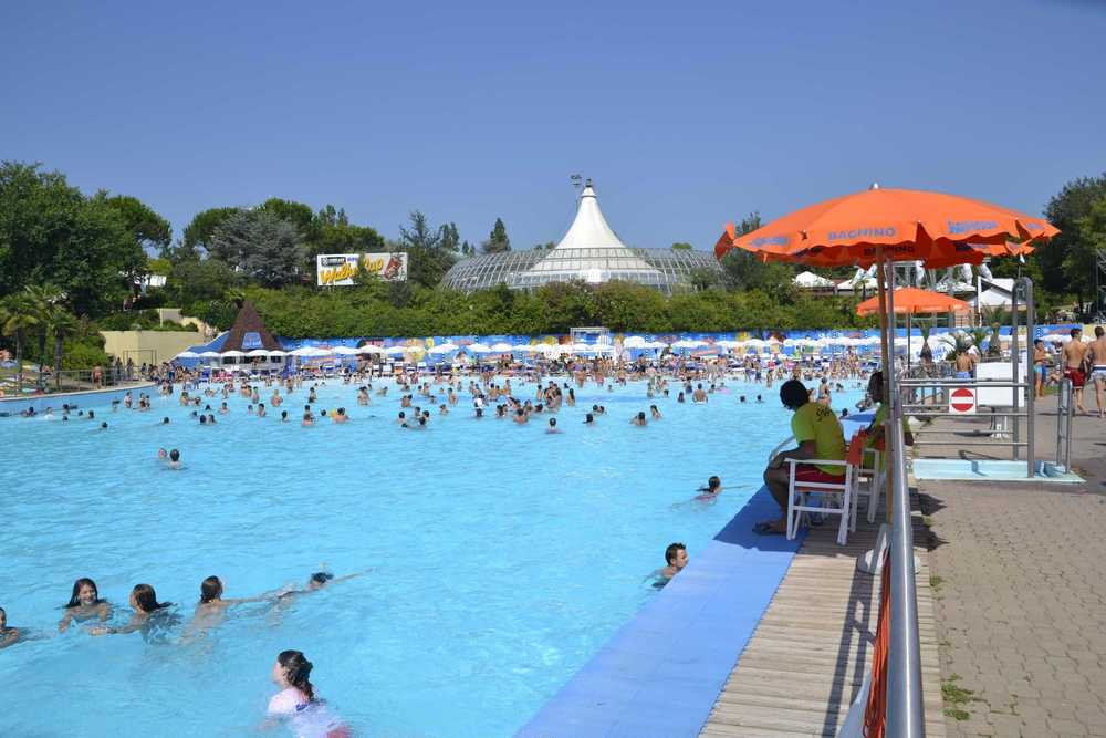 Přeplněný vlnový bazén v Aquafanu v Riccione, kde plavci splývají s tyrkysovou vodou pod rozpáleným italským sluncem.