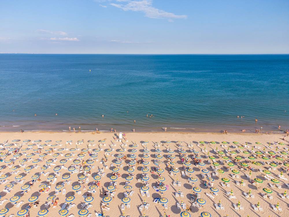 Letecký pohled na pláž Bibione s řadami žlutomodrých slunečníků a lehátky u mělkého Jaderského moře