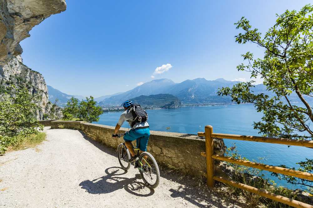 Cyklista na horském kole projíždí kamennou cestou nad jezerem Garda s výhledem na Alpy v létě