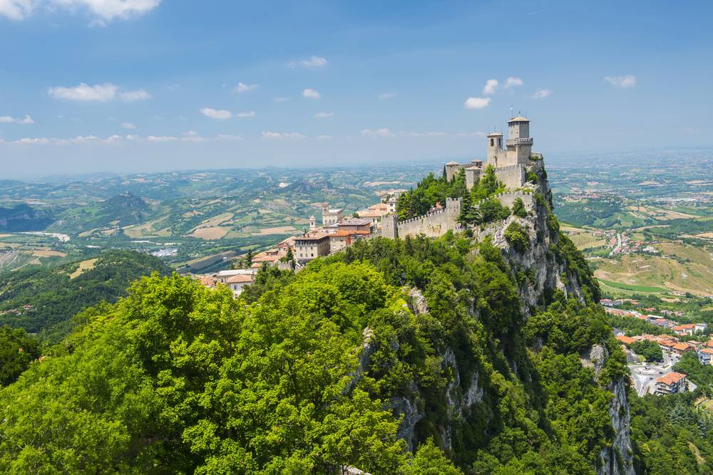 Středověká pevnost Guaita na vrcholu skalnatého Monte Titano v San Marinu, obklopená zelenými stromy s výhledem do italské nížiny